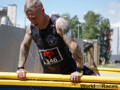 En tatuerad deltagare i Gatti Training-linne tar sig över ett hinder i ett hinderlopp.