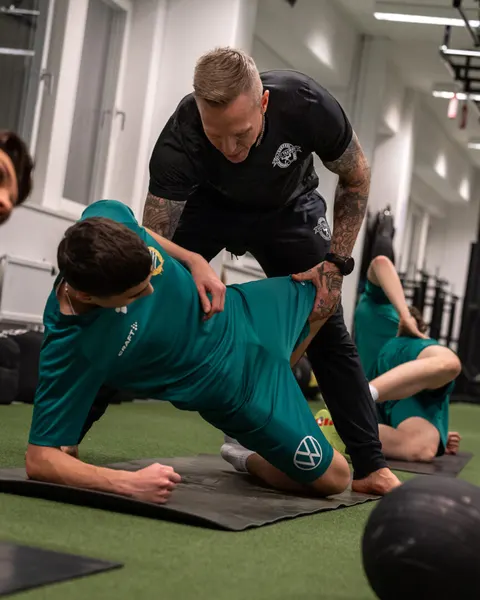 En coach justerar en ung fotbollsspelares position i en övning på mattan.