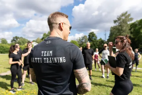 En coach i Team Gatti Training-tröja pratar med en grupp under ett utomhuspass.
