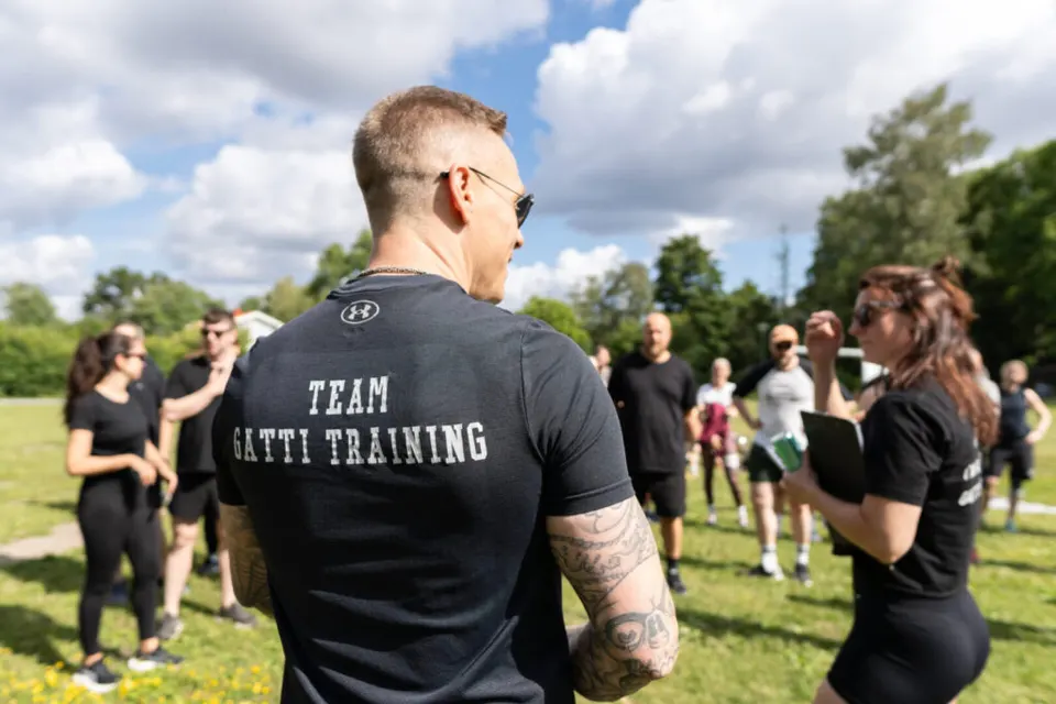En coach i Team Gatti Training-tröja pratar med en grupp under ett utomhuspass.