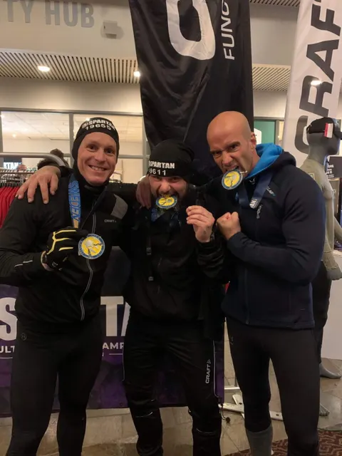 Tre deltagare med medaljer i munnen efter ett Spartan-lopp.