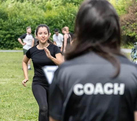 En kvinna springer mot en coach på en gräsmatta under ett utomhuspass.