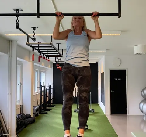 En kvinna gör en chins i en träningsställning i gymmet.