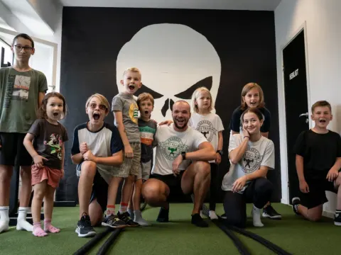 En coach och en grupp barn gör glada miner framför dödskallemålningen i gymmet.