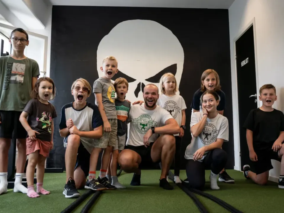 En coach och en grupp barn gör glada miner framför dödskallemålningen i gymmet.