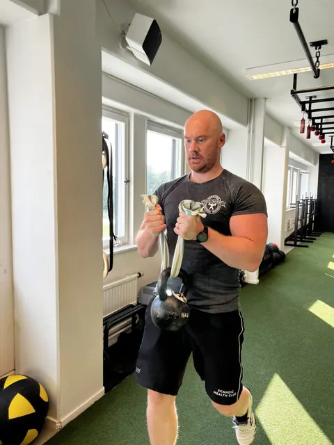 En man gör en utfallsgång med en kettlebell i händerna.