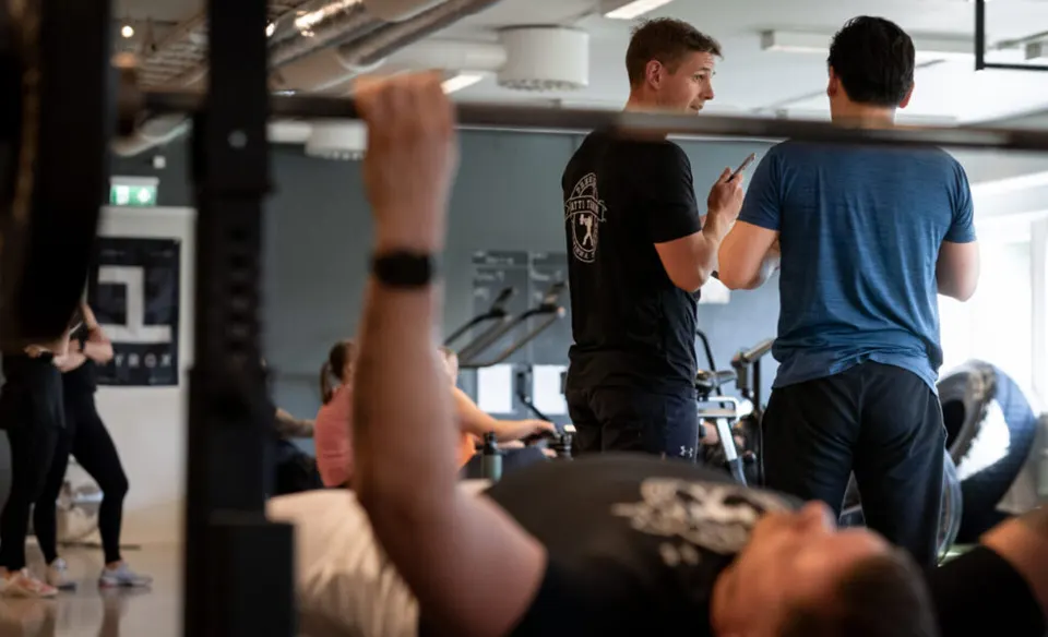 En coach hjälper en medlem med träning vid en bänk.