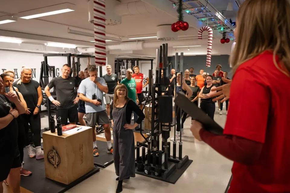 Medlemmar samlade i det juldekorerade gymmet lyssnar på en coach med anteckningsblock.
