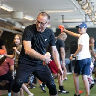 En man skrattar mitt i en lekfull övning under ett familjepass i gymmet.