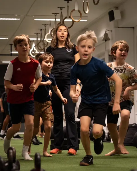 Barn springer i grupp på konstgräsbanan medan en coach följer dem.