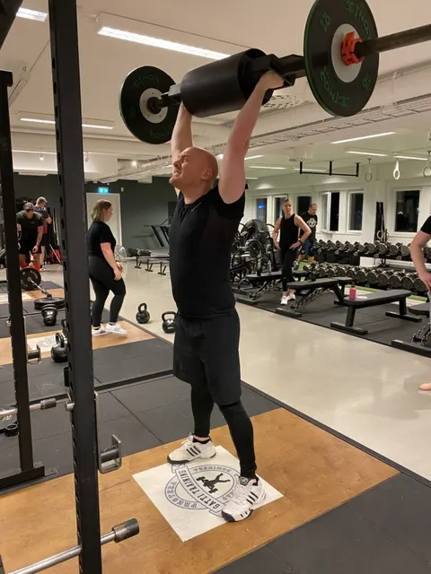 En man lyfter en skivstång över huvudet i gymmet.
