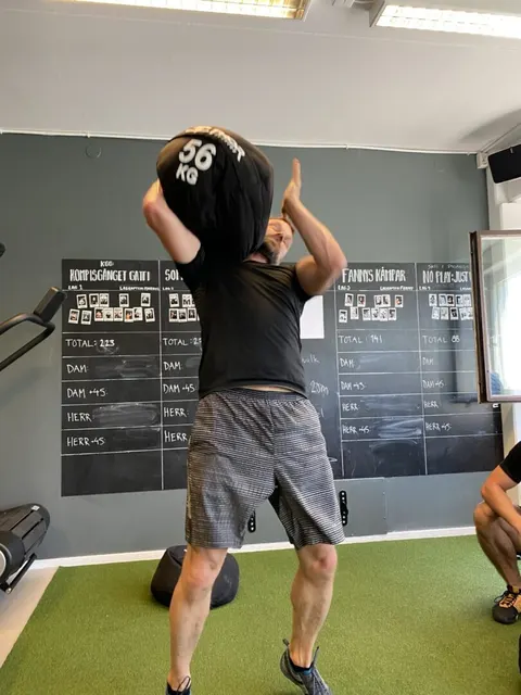 En man lyfter en tung boll märkt 56 kg framför svarta tavlan i gymmet.