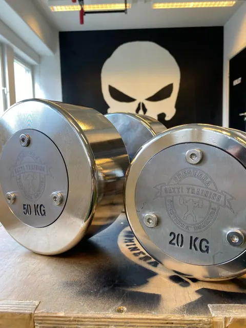 Två blanka hantlar på 50 och 20 kg framför dödskallemålningen i gymmet.