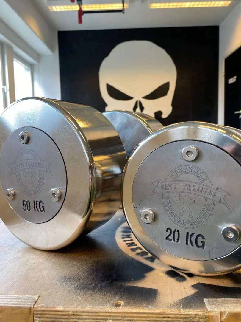 Två blanka hantlar på 50 och 20 kg framför dödskallemålningen i gymmet.