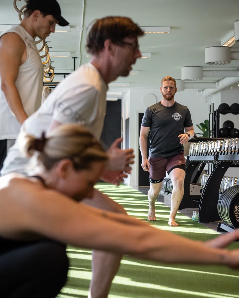 Medlemmar tränar tillsammans på gymmet med en coach i bakgrunden.
