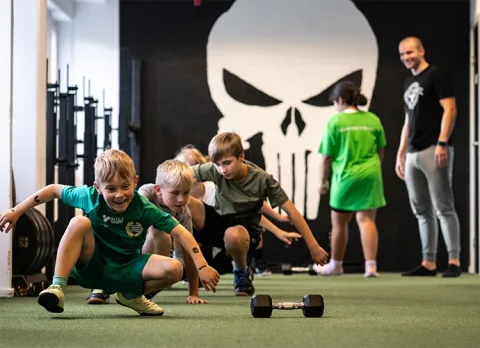 Barn gör björngång på konstgräset medan coachen följer gruppen.